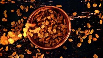 Raisins fall into a wooden bowl on the table. Top view. Against a dark background. Filmed is slow motion 1000 fps. video