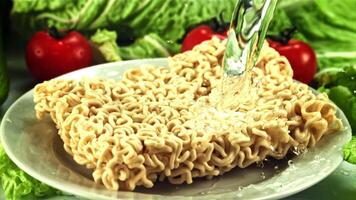 A jet of water falls on the dry noodles in the plate. Against the backdrop of tomatoes and lettuce. Filmed on a high-speed camera at 1000 fps. video