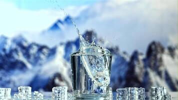 een ijs kubus valt in een glas van water met spatten. tegen de backdrop van bergen. gefilmd is langzaam beweging 1000 fps. video