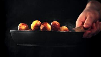 A man's hand tosses fried potatoes in a frying pan. On a black background. Filmed is slow motion 1000 fps. video