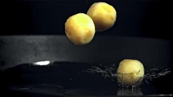 pelado patatas otoño dentro un fritura pan con salpicaduras de aceite. en un negro antecedentes. filmado en un alta velocidad cámara a 1000 fps. video