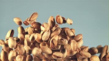 pistachenoten vlieg omhoog en vallen omlaag. Aan een blauw achtergrond. gefilmd Aan een hoge snelheid camera Bij 1000 fps. video