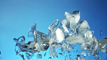 Pieces of ice with splashes of water soar up and fall. On a blue background. Filmed is slow motion 1000 fps. video