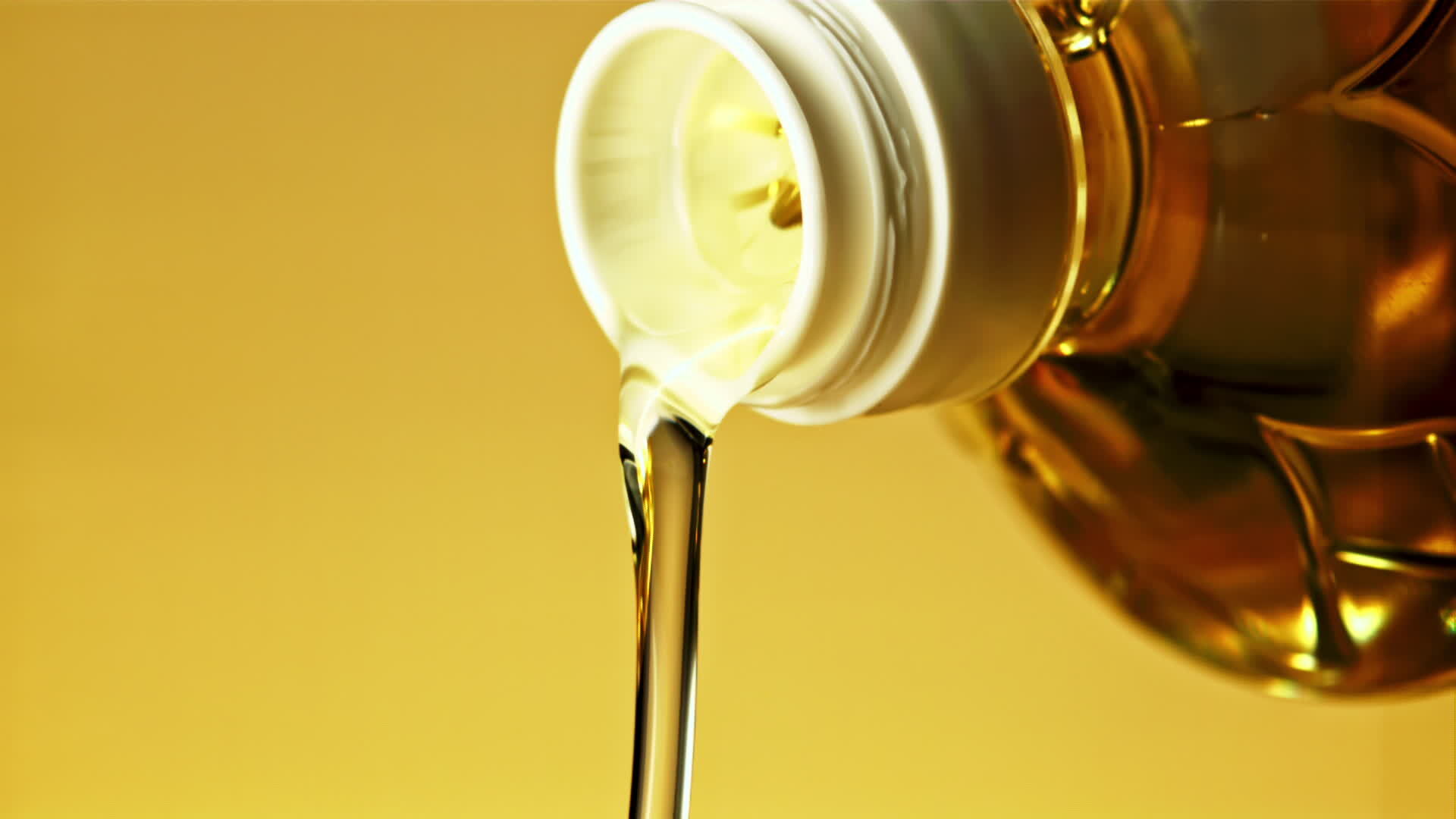A stream of olive oil pours out of the bottle. On a yellow background