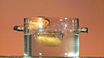 Fresh unpeeled potatoes fall into a pot of water splashes. On a pink background. Filmed is slow motion 1000 fps. video