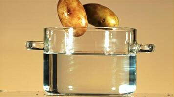 Fresh potatoes fall into a pot of water with splashes. On an orange background. Filmed on a high-speed camera at 1000 fps. video