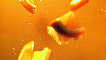 Pieces of fresh orange fall into orange juice with splashes. Macro background. Filmed on a high-speed camera at 1000 fps. High quality FullHD footage video