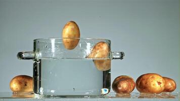 Fresh potatoes fall into a pot with splashes of water. On a blue background. Filmed is slow motion 1000 fps. video