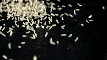 A pile of uncooked rice falls on the table. On a black background. Filmed is slow motion 1000 fps. video