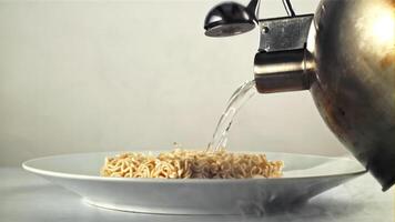 caldo acqua a partire dal il teiera versa su il asciutto tagliatelle. su un' bianca sfondo. girato su un' alta velocità telecamera a 1000 fps. video