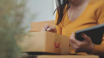 Shipping shopping online ,young start up small business owner writing address on cardboard box at workplace.small business entrepreneur SME or freelance asian woman working with box at home video