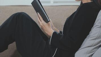 Asian working woman wearing black shirt and writing journal on small notebook on the table at indoor cafe. Woman notes and drinking coffee at cafe. Working from anywhere concept. video