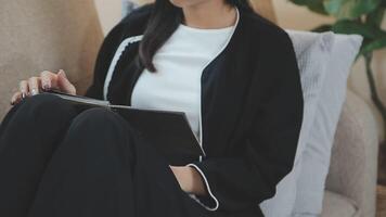 Asian working woman wearing black shirt and writing journal on small notebook on the table at indoor cafe. Woman notes and drinking coffee at cafe. Working from anywhere concept. video