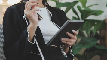 Asian working woman wearing black shirt and writing journal on small notebook on the table at indoor cafe. Woman notes and drinking coffee at cafe. Working from anywhere concept. video