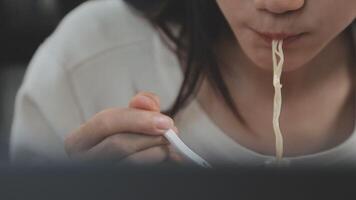 dichtbij omhoog Aziatisch vrouw aan het eten lekker heet en pittig ogenblik noodle gebruik makend van eetstokjes en schaal. aan het eten Aan de tafel video