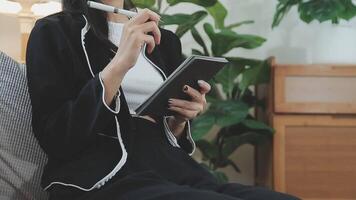 Asian working woman wearing black shirt and writing journal on small notebook on the table at indoor cafe. Woman notes and drinking coffee at cafe. Working from anywhere concept. video