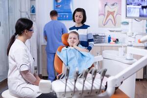 Little girl with painful expression showing dentist where her tooth hurts during dental check up. Child with her mother during teeth check up with stomatolog sitting on chair. photo
