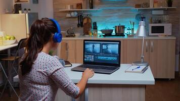 Professional colorist working in video footage during post production. Videographer editing audio film montage on modern device, laptop sitting on desk in modern kitchen in midnight photo