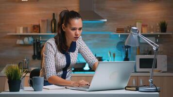 Busy woman work at night from home and taking notes from laptop writing on notebook. Busy focused employee using modern technology network wireless doing overtime for job reading typing, searching photo