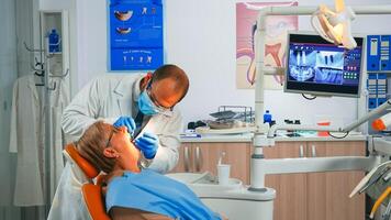 Oral surgeon checking with mirror dental crowns installed in senior woman mouth. Nurse lighting the lamp, doctor speaking to patient sitting on stomatological chair, preparing for surgery. photo