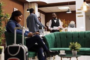 Hotel front office team welcoming and registering guest at reception desk, African American man receptionist talking with tourist completing check-in or check-out. People arriving at resort photo