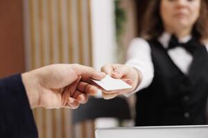 Hotel worker gives access card to guest, businessman travelling for work arrives at front desk reception for check in. Receiving room key to relax before upcoming business meeting. Close up. photo