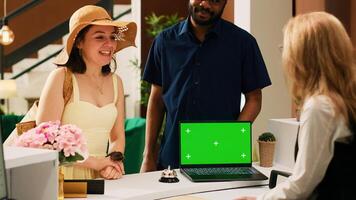 Receptionist welcoming tourists and using greenscreen display on laptop, talking to couple for check in procedure. Front desk staff working with chroma key mockup template in lobby. photo