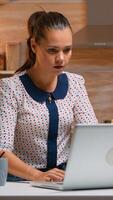 Business woman working from home sitting in the kitchen typing on laptop late at night. Busy focused employee using modern technology network wireless doing overtime for job reading writing, searching photo