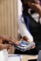 Hotel guest using credit card to pay for stay while registering at front desk, close up. Male hand making contactless payment during check-in, paying for room with nfc technology photo