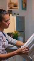 Freelancer architect working in 3D software to elaborate buildings design sitting at kitchen desk at night. Engineer artist creating and studying in office holding scale model, determination, career. photo