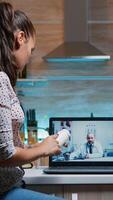 Telemedicine consultation during covid pandemic at night, woman sitting in front of laptop in the kitchen. Sick lady discussing during virtual consultation about symptoms holding bottle of pills photo