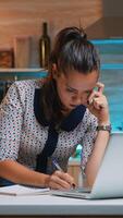 Busy woman work at night from home and taking notes from laptop writing on notebook. Busy focused employee using modern technology network wireless doing overtime for job reading typing, searching photo
