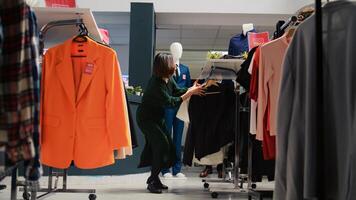 Customer checking fashion items on racks in department store, making purchases at shopping center during black friday promotions. Client buying clothing items from hangers. Handheld shot. photo