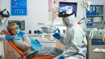 Dentist doctor with protection equipment talking with old patient before consultation during covid-19 epidemic. Concept of new normal dentist visit in coronavirus outbreak wearing protective suit and face shield photo