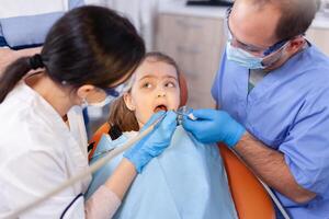 Child with mouth open in the course of caries treatment looking at dentist. Mother with her kid in stomatology clinic for teeth examine using modern instruments. photo