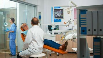 Dental specialist talking with senior patient in stomatology chair before examination. Elderly woman explaining dental problem and toothache. Treatment dentistry prevention photo