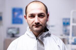 Close up of exhausted doctor in dental office looking on camera in the course of covid19 pandemic. Portrait of tired stomatologist wearing coronavirus ppe suit looking at camera. photo