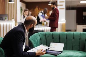 Businessman review documents in lobby at hotel, waiting to do check in procedure and killng time with office work. Entrepreneur attending official meeting and looking over speech notes. photo