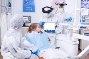 Dentist dressed in ppe suit using digital device with chroma key Medical specialist in oral hygine holding tablet pc with copy space available during global pandemic with covid19. photo