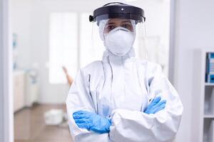 Stressed doctor with arms crossed in hazmat suit during coronavirus outbreak. Medical personal dressed in protection equipment against infection with covid-19 during global pandemic. photo