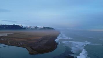 Aerial view of icelandic coastline with famous black sand beach and nordic scenery, snowy mountains and hills. Beautiful altantic ocean shore with roadside, natural panoramic view. Slow motion. photo