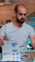 Focused busy entrepreneur checking graphics from clipboard using laptop looking on laptop working from home on midnight. Busy focused employee using modern technology network wireless photo