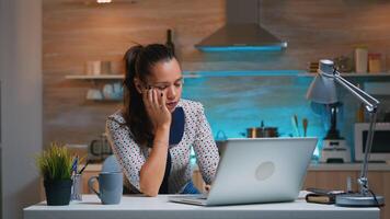 Exhausted remote woman napping on chair waking up working on laptop sitting in kitchen late at night.Busy employee using modern technology network wireless doing overtime reading closing eyes sleeping photo
