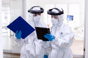 Overworked doctors team working together wearing ppe suit in hospita. Medical colleagues wearing professional gear against infection with coronavirus as safety precauition. photo