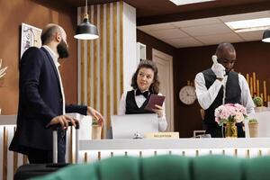 Check in process at reception counter. Front desk staff verifying passport and documents for identification in lobby, white collar worker waiting to enter room on business trip. photo