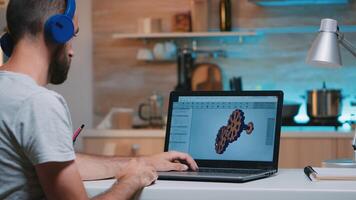 Man architect with wireless headset using laptop while working at home at night sitting in the kitchen. Industrial employee studying prototype idea on personal computer showing cad software on display photo