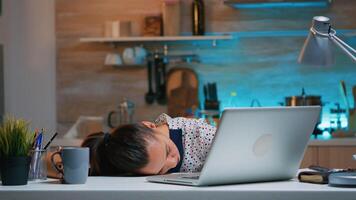 Overworked tired woman working from home felling asleep on desk in front of laptop. Busy focused employee using modern technology network wireless doing overtime closing eyes and sleeping on table. photo