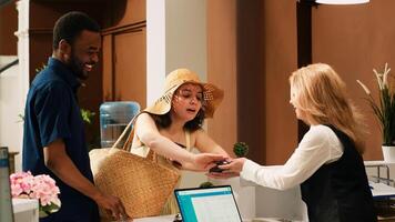 Hotel guests paying for room reservation, using credit card for payment on pos terminal at front desk reception. Couple on summer holiday making transaction upon their arrival. Handheld shot. photo