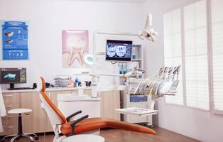 Dental chair and other accesorries used by dentist in empty cabinet. Stomatology cabinet with nobody in it and orange equipment for oral treatment. photo