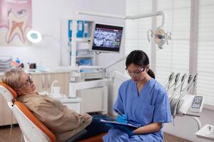 Dental assistant completing questioner during oral checkup of elderly patient. Senior woman talking with medical nurse in stomatology office about teeth problem. photo